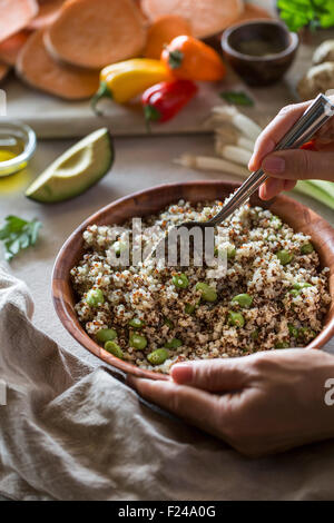 Une femme est de mélanger le quinoa avec edamame écossées, au procédé de fabrication d'un bol d'alimentation. Banque D'Images