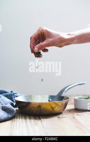 Saupoudrer de fines herbes dans une casserole en cuivre Banque D'Images