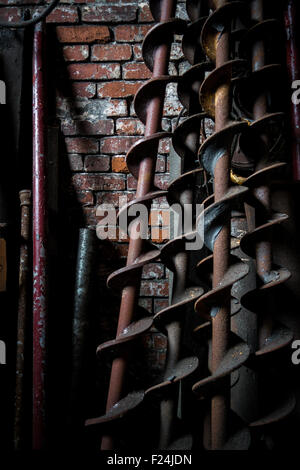 Grande vis ou drill bits appuyer contre un mur de brique rouge, baigné dans l'ombre Banque D'Images