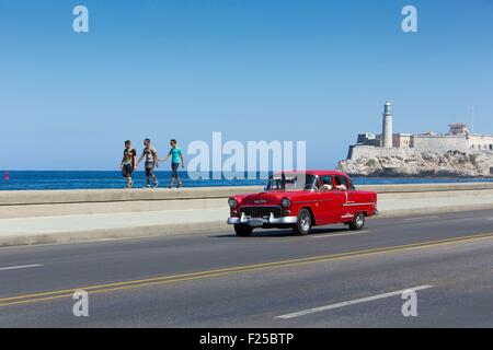 Cuba, Ciudad de la Habana Province, La Havane, voiture américaine sur le Malecon et le phare du Castillo de los Tres Reyes Magos dans l'arrière-plan Banque D'Images