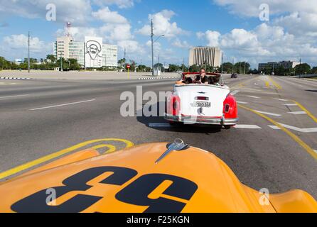 Cuba, Ciudad de la Habana Province, La Havane, Vedado, quartier de la Plaza de la Revolucion (place de la Révolution), voiture américaine et les touristes avec la façade d'un bâtiment public représentant Camilo Cienfuegos en arrière-plan Banque D'Images