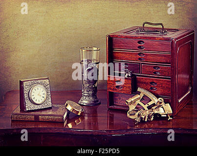 Vintage still life, bijoux boîte en bois, horloge, livre ancien, sextant et d'étain et de verre gobelet Banque D'Images