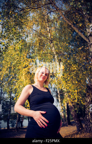 Portrait d'une jeune et belle femme enceinte parmi les arbres colorés Banque D'Images