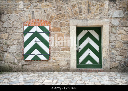 Vieux Mur de pierre avec fenêtre et porte en bois peint en blanc et vert. Banque D'Images