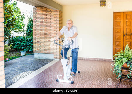 Personnes âgées L'octogénaire homme perdre du poids ne cesse de monter en faisant un vélo sur le patio de la chambre Banque D'Images