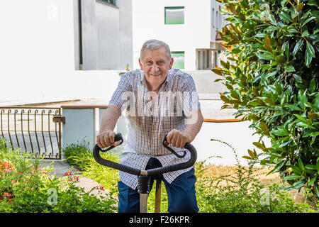 Personnes âgées de sexe masculin ne cesse de monter par l'octogénaire doing exercise bike sur le jardin de la maison Banque D'Images