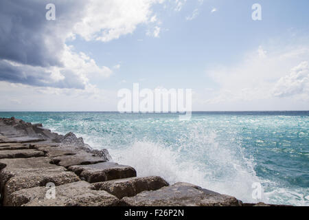 Vagues se brisant sur la digue en face d'un ciel bleu avec des nuages Banque D'Images