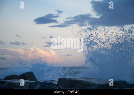 Vagues se brisant sur la digue devant un coucher de soleil avec des nuages ciel Banque D'Images