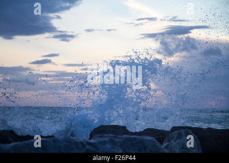 Vagues se brisant sur la digue devant un coucher de soleil avec des nuages ciel Banque D'Images