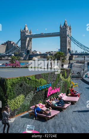 Les gens se détendre dans le soleil d'été à Londres Riviera pop up restaurant, avec tour emblématique Bridge en arrière-plan, en Angleterre, Royaume-Uni Banque D'Images