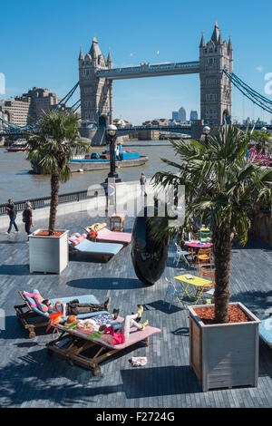 Les gens se détendre dans le soleil d'été à Londres Riviera pop up restaurant, avec tour emblématique Bridge en arrière-plan, en Angleterre, Royaume-Uni Banque D'Images