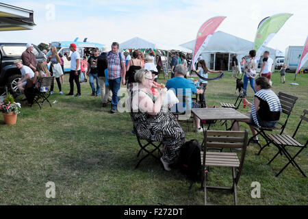 Femme plus âgée assise à l'extérieur à la table de pique-nique avec la foule mangeant des beignets de beignets au salon agricole au Royaume-Uni KATHY DEWITT Banque D'Images