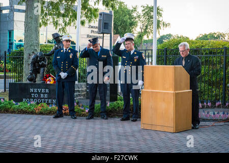 Merrick, New York, USA. 11 septembre 2015. À podium, Deacon JOE ZUBROVICH, Curé d'ars de l'Église catholique romaine en Merrick, invocation commence comme firefigthters 3 Merrick et NYC, près de statue 9/11 momument, commencer à enlever leurs chapeaux blanc de l'uniforme de cérémonie commémorative au cours de Merrick Merrick pour les pompiers volontaires et les résidents qui sont morts en raison d'attentats terroristes à New York Tours Jumelles. Ex-Chief Ronnie E. Gies, du Merrick F.D. et FDNY Squad 288 Ex-Captain, et Brian E. Sweeney, du Merrick F.D. et FDNY Rescue 1, est mort en réponse à des attaques du 11 septembre 2001. © Ann E Parry/Alam Banque D'Images