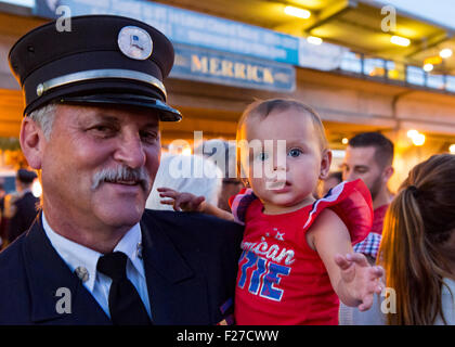 Merrick, New York, USA. 11 septembre 2015. RILEY E. GIES, one-year-old fille de Ronnie, chef des pompiers qui sont morts des gies e répondre aux attaques terroristes de New York le 11 septembre 2001, est détenu par CRAIG MALTZ, un pompier bénévole Bellmore, après Merrick Merrick Cérémonie commémorative pour les pompiers volontaires et les résidents qui sont morts en raison d'attentats terroristes à New York Tours Jumelles. Credit : Ann E Parry/Alamy Live News Banque D'Images