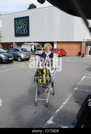 Femme d'âge moyen avec chariot et lourds sacs de magasinage magasin Marks & Spencer en voiture de chargement Banque D'Images