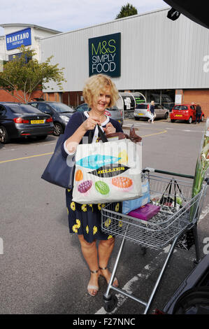 Femme d'âge moyen avec chariot et lourds sacs de magasinage magasin Marks & Spencer en voiture de chargement Banque D'Images