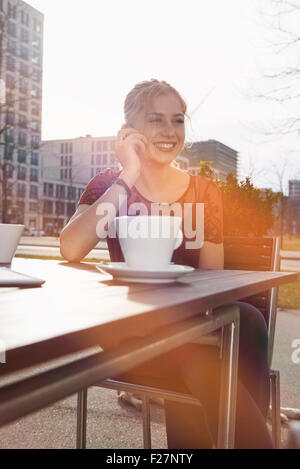 Young Woman talking on a mobile phone at sidewalk cafe, Munich, Bavière, Allemagne Banque D'Images