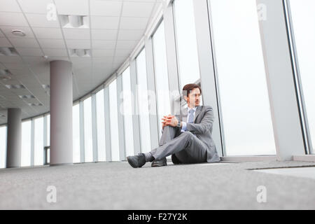 Businessman sitting on floor in office fenêtre proche Banque D'Images
