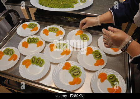 Un traiteur prépare des plats de dessert avec des tranches de kiwi et orange. Banque D'Images