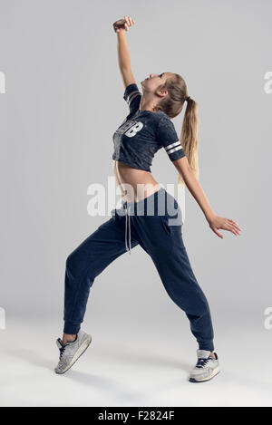 Tourné sur toute la longueur d'une jeune femme danseuse hip hop dans une position des pieds contre le mur gris. Banque D'Images