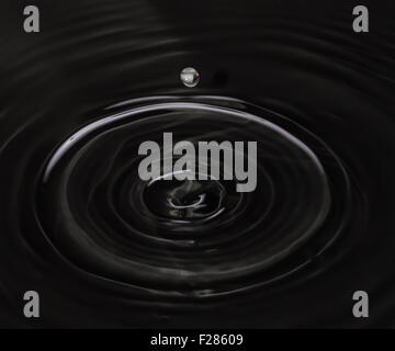 Goutte d'eau tombant dans l'eau noire Banque D'Images