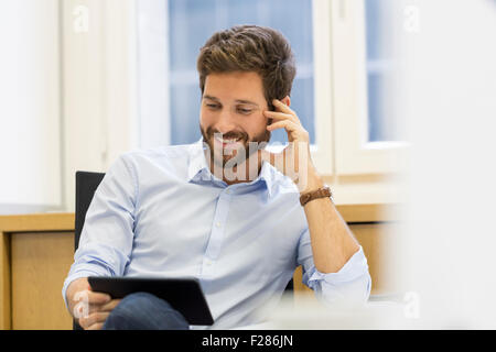 Cheering businessman using digital tablet in office Banque D'Images