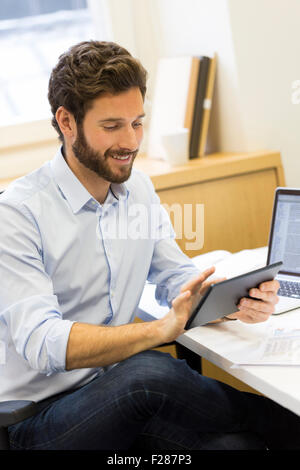 Jeune homme barbu en consultation en bureau ordinateur tablette. Banque D'Images