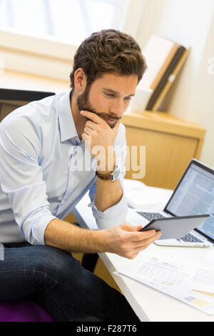 Jeune homme barbu en consultation en bureau ordinateur tablette. Banque D'Images