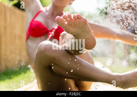 Femme refroidissement dans jardin avec les projections d'eau sprinkleur autour de gouttes Banque D'Images