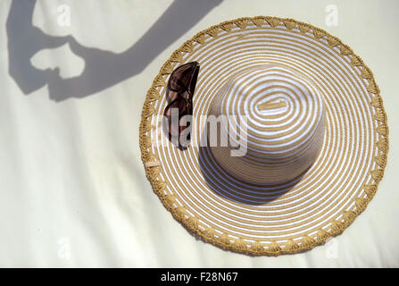 L'ombre de deux mains formant un coeur à côté d'un chapeau de soleil et des lunettes de soleil. Banque D'Images