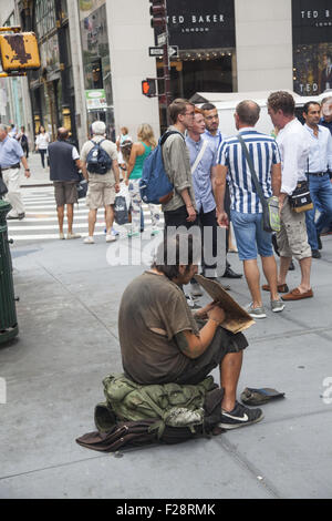 Sans-abri assis sur le trottoir et la mendicité parmi les touristes et les New-Yorkais à Midtown Manhattan. Banque D'Images