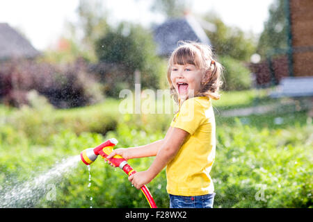 Happy girl verse de l'eau d'un tuyau flexible dans jardin Banque D'Images