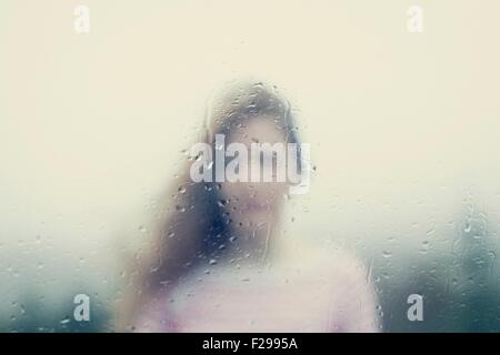 Image floue d'une femme par une fenêtre des pluies Banque D'Images
