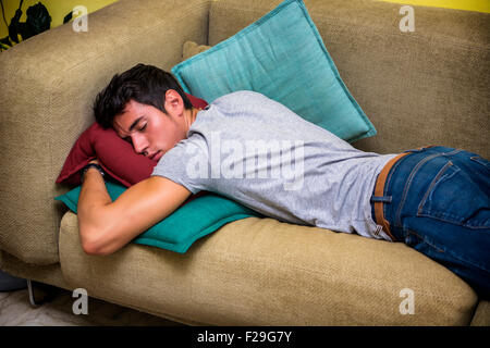 Trois quart d'un jeune homme ivre de dormir sur le canapé dans le salon d'accueil. Banque D'Images