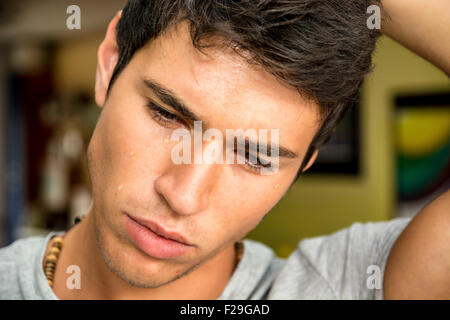 Close up visage d'un beau jeune homme pensif avec des larmes sur son visage, regardant vers le bas, inquiets ou tristes. Banque D'Images