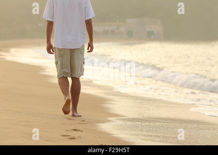 Vue arrière d'un homme qui marche et laisser des empreintes de pas sur le sable d'une plage au coucher du soleil Banque D'Images