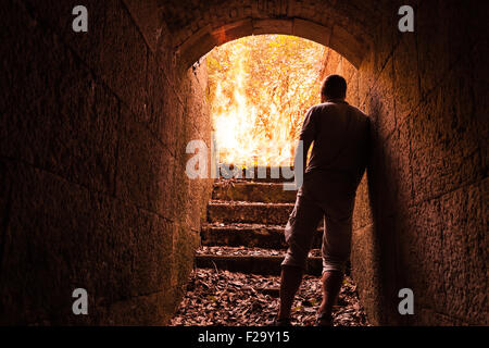 Jeune homme est en pierre sombre tunnel avec grand feu dans la fin Banque D'Images