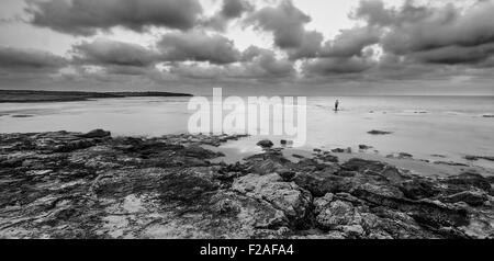 Pêcheur solitaire debout dans l'eau au lever du soleil, à la plage Dor, Israël en noir et blanc Banque D'Images