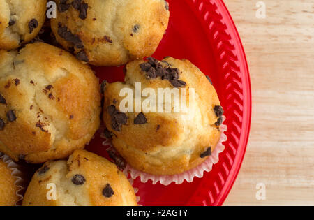 Haut de page Fermer la vue des petits petits muffins aux pépites de chocolat sur une plaque rouge au-dessus d'une table en bois éclairé par la lumière naturelle. Banque D'Images