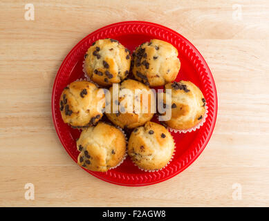 Vue de dessus de plusieurs petits muffins aux pépites de chocolat fraîchement cuits sur une plaque rouge au-dessus d'une table en bois naturel avec lumineux Banque D'Images