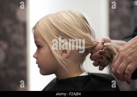 Coupe Coiffure féminine et le brossage du jeune enfant fille blonde cheveux dans le salon de coiffure Banque D'Images