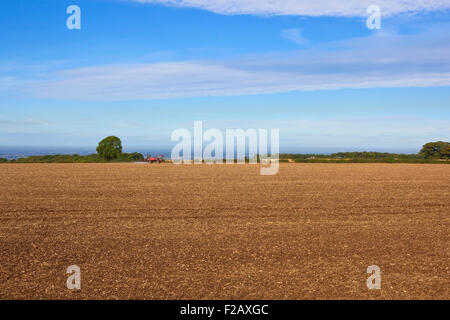 Un paysage agricole avec un pulvérisateur rouge travaillant dans un champ cultivé sur les Yorkshire Wolds en septembre. Banque D'Images