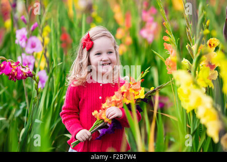 Little girl holding glaïeul fleurs''. Préparation de l'enfant des fleurs fraîches dans le jardin. Les enfants le jardinage en automne. Banque D'Images