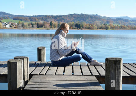 Fille de la lecture d'un comprimé sur la jetée en bois sur un lac. La Suisse Banque D'Images