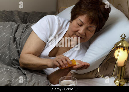 Close up of senior woman, prenant la médecine en bouteille, tandis que dans le lit. Le concept de maladie. Banque D'Images