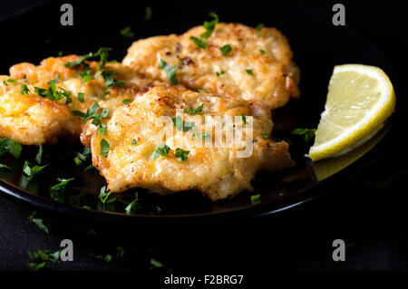 Escalope de poulet frit avec du citron sur la plaque sombre Banque D'Images