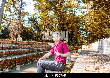 Beau et charismatique Caucasian sportsman de quarante avec cheveux gris polo porter du rouge foncé et un pantalon de lin indique lui-même assis sur l'ancienne cité médiévale de mesures du Canal de l'usine dans l'Émilie-Romagne en Italie Banque D'Images