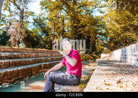 Beau et charismatique Caucasian sportsman de quarante avec cheveux gris polo porter du rouge foncé et un pantalon de lin vous invite à être au calme tout en étant assis sur l'ancienne cité médiévale de mesures du Canal de l'usine dans l'Émilie-Romagne en Italie Banque D'Images