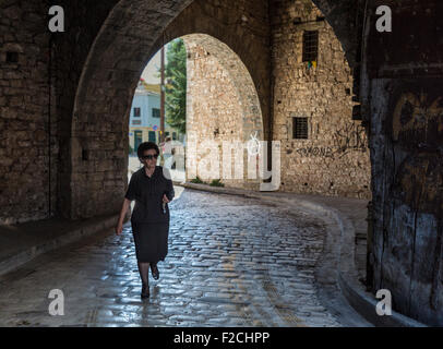 Femme grecque en robe noire sortant de la vieille ville de Ioannina via un passage voûté dans les murs de la ville Banque D'Images