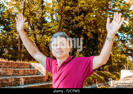 Beau et charismatique Caucasian sportsman de quarante avec cheveux gris polo porter du rouge foncé et un pantalon de lin est raising arms, assis sur l'ancienne cité médiévale de mesures du Canal de l'usine dans l'Émilie-Romagne en Italie Banque D'Images